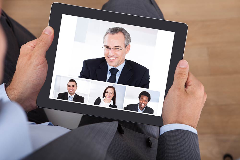 person holding a tablet with four video meeting participants